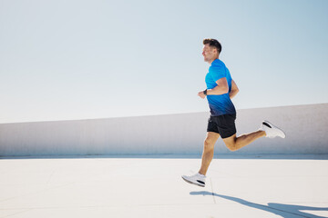 Energetic Man Sprints Across a Sunlit Rooftop in a Vibrant Blue Shirt, Showcasing Determination and...
