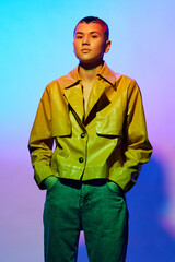 confident woman in yellow jacket and green pants stands against colorful gradient background with hands in pockets, short hair, and calm expression, vibrant lighting