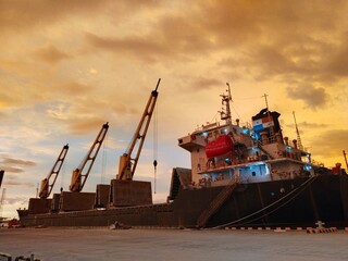 cargo ship in port with sunset full of cloud 