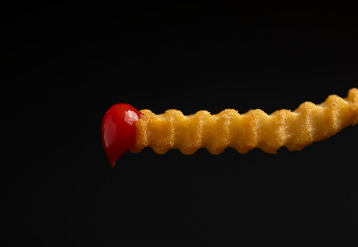 Close up of one golden French fry in tomato ketchup on a black background