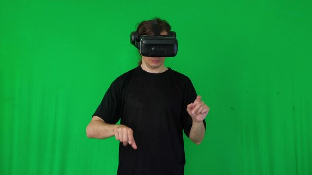 A mid-shot captures an interactive and engaging mood as a person wearing a VR headset makes open-hand gestures, suggesting immersion in a virtual environment or game, against a green screen background