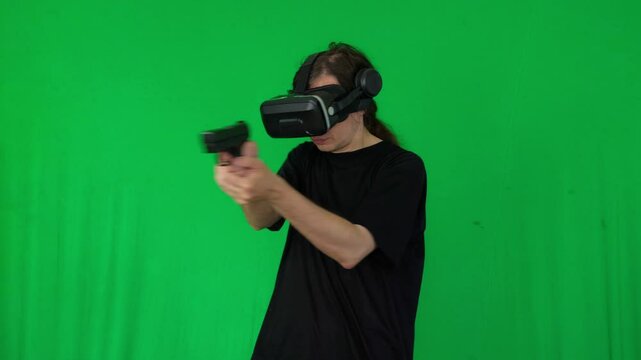 A mid-shot captures an intense and action-packed mood as a person wearing a VR headset aims a handgun, suggesting immersive virtual reality gaming or simulation, against a green screen background
