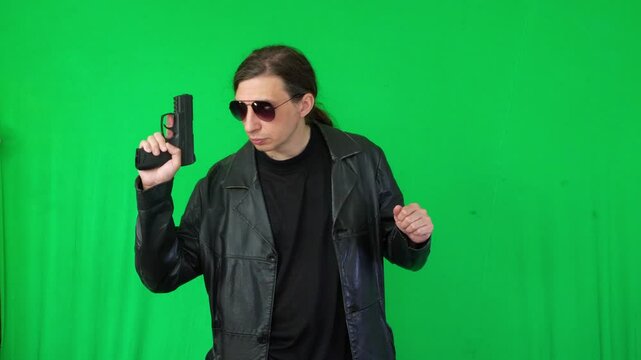 A mid-shot captures an intense and determined mood as a man in a leather jacket and sunglasses aims a handgun, focused on a target, against a green screen, ideal for action themes