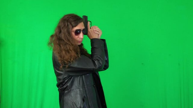 A mid-shot captures a serious and ready mood as a man in a leather jacket and sunglasses holds a handgun with both hands, looking directly at the camera, against a green screen