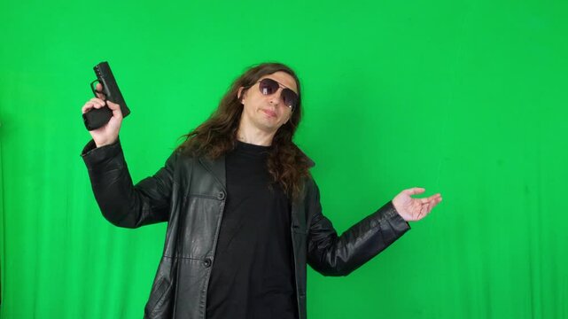 A mid-shot captures a serious and ready mood as a man in a leather jacket and sunglasses holds a handgun with both hands, looking directly at the camera, against a green screen