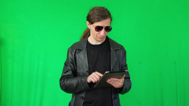 A mid-shot captures a happy and expressive mood as a man in a leather jacket and sunglasses holds a tablet and gestures enthusiastically, suggesting a positive reaction or presentation