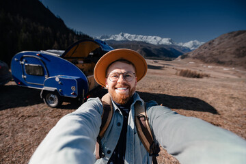 Plakat Young happy man hipster traveler making selfie background camper car on mountain. Concept one life adventure trip, vacation.