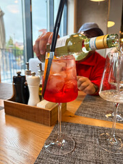 A man pours white wine from a bottle into a glass while sitting in a cozy cafe, capturing a moment...