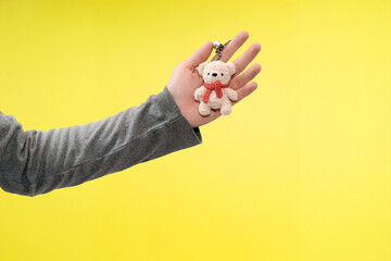 hand holding cute bear keychain in yellow background