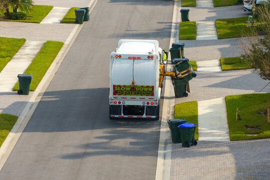 Fototapeta Garbage removal in residential area. Waste truck loading household rubbish while driving on suburban street