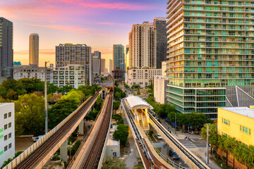 Urban railroad for public transit lines stretches across Miami Brickell downtown in Florida, USA. Setting sun casting light on city high-rise buildings and train route
