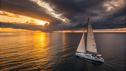 White sailboats sailing into the ocean at sunset