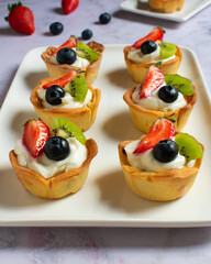 Tartaletas de crema de queso y fruta fresca en bandeja de cerámica blanca