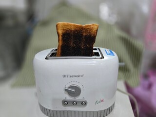 Burnt toast slices sticking out of modern toaster. Burnt bread from overheating the white toaster. Burnt bread in toaster on blurred background. Heat too high will cause the bread to turn black.
