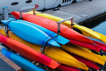 Row of bright, colorful kayaks on a storage rack at a pier in Norway. Concept of summer travel, adventure, and water sports rental.