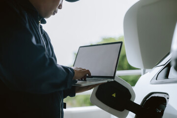 Technician uses laptop to diagnose electric vehicle during charging process in outdoor setting