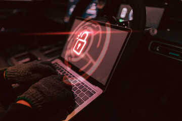 Individual in a hooded garment using a laptop inside a parked vehicle to access secure data at night