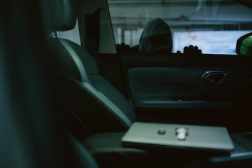 Fototapeta premium Laptop on car seat in dark parking garage with shadowy figure in background during evening hours