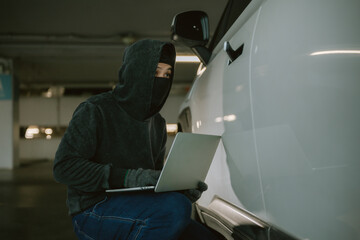 Individual engaged in suspicious activity with a laptop near a vehicle in a parking garage during night hours