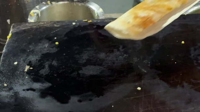 "Close-up view of dosa cooking on hot tawa with golden brown texture forming while steaming on traditional Indian iron skillet during street food preparation"

