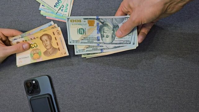 Hands exchanging Chinese yuan banknotes with dollars and euros on table close up top view international currency exchange payment transaction and global finance concept