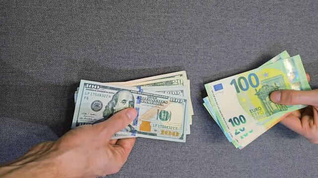 Hands counting US dollar banknotes and holding euro cash currency exchange transaction close up top view financial payment concept with different currencies on grey background