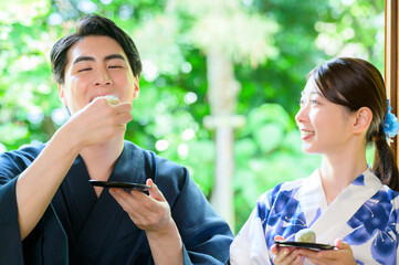 浴衣姿の男女が和菓子を分かち合いながら笑い合う夏の光景