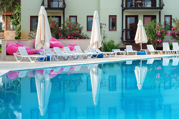 Empty swimming pool with sunbeds and white umbrellas