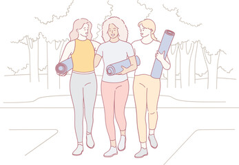 Three close friends are walking together while carrying their yoga mats, eager for an exciting outdoor yoga session