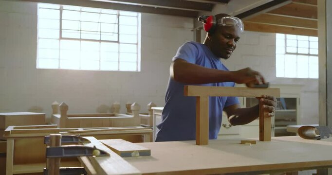 African American man sanding T-shaped frame after coworker pointing rough spot in bright workshop