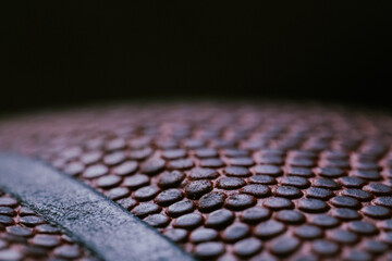 Extreme Close-up detail macro shot of a textured leather dark orange basketball showing the individual dimples on the ball and the black rubber stripes on a black background. Sports Equipment.