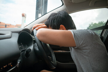 Asian man slumping over steering wheel in exhaustion, bad traffic