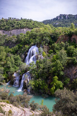 A cascade of water falling through the lush vegetation, Campillo waterfall, in the natural park of the Alto Tajo in Guadalajara, vertical