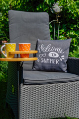 Scene with two coffee cups in a special wooden cup holder, a chair and a cushion in a garden.