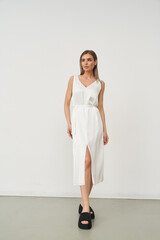 Elegant woman in fitted white dress with a front slit, posing confidently, wearing black platform...