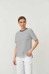 Stylish woman poses indoors in casual striped top and white pants