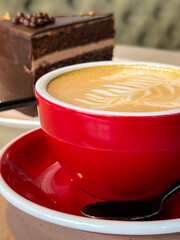 Red cup of cappuccino and chocolate cake. Enjoy your meal!