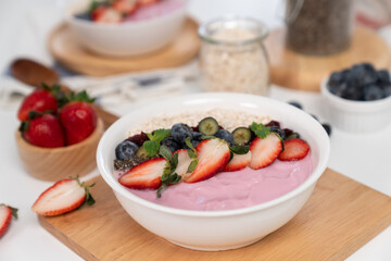 Presented by fruits putting yogurt toppings with strawberry, berry, oats, raisins and chia seed decorated by peppermint in white blow. Pink background. Set of healthy dairy product choice. Pecuniary.