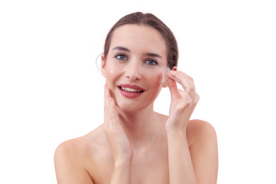 Portrait of happy young woman with a natural, no makeup look, applying silicone under eye patches and smiling while looking at the camera. Skincare concept for dark circles, isolated white background