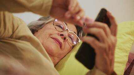 Close-up of Senior Woman Relaxing in Bed While Using Smartphone to Stay Connected and Informed