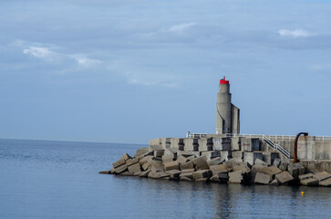 Modern concrete pier with a red lighthouse stands on the tranquil coastline, symbolizing navigation...
