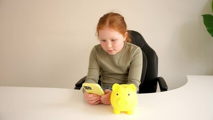 Child interacts with smartphone while sitting at desk with yellow piggy bank, showcasing money management skills