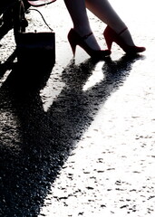 A woman's legs and red heels are reflected in a wet surface, with a purse nearby.