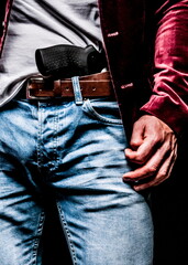A person is wearing a red velvet jacket, blue jeans, and a brown belt. A black handgun is holstered...
