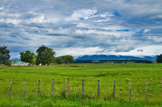 Green meadows, old fence, simple farmhouse and dark hills under a dramatic sky. Manawatu region, North Island, New Zealand, close to Fielding.
