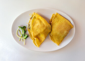 Savory crepes with ham and mushroom filling, garnished with fresh microgreens. Top-down view on a white plate.Delicious breakfast or brunch: Two French-style savory crepes