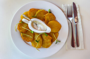 Traditional draniki, potato pancakes, served with sour cream and garnished with microgreens.Crispy golden potato pancakes served with sour cream sauce on a white plate for a savory breakfast or brunch