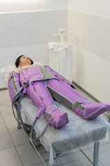 Obraz premium Woman patient in pressotherapy procedure lying on medical bed relaxing. Hardware cosmetology technique used against puffiness, cellulite. Affects lymphatic system with compressed air supplied in suit.