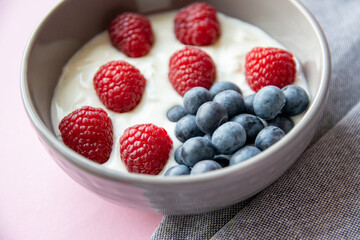 Gray bowl and natural yogurt with red and blue berries on the pink background.