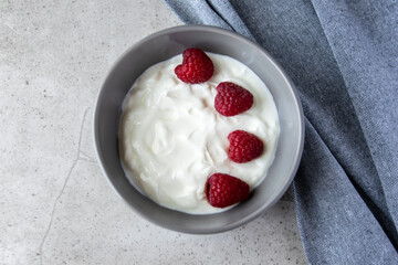 Gray bowl and natural yogurt with red berries on the stone marble table.